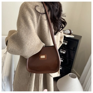 Détail d'un sac bandoulière marron foncé vintage avec logo doré sur manteau en laine