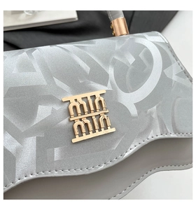 Detail of silver-grey textured handbag with gold metal logo and white stitching details