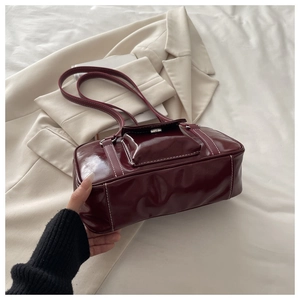 Detail of burgundy glossy leather shoulder bag with white contrast stitching and silver buckle