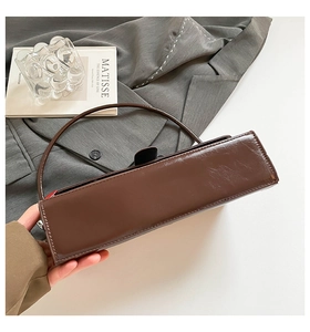 Detail of a dark brown glossy patent leather baguette bag with minimalist stitching