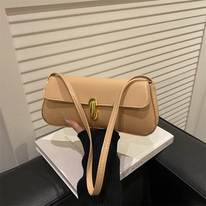 Beige patent leather shoulder bag with gold metal clasp on white book background