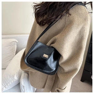 Détail d'un sac à bandoulière en cuir noir brillant avec plaque dorée porté sur un manteau