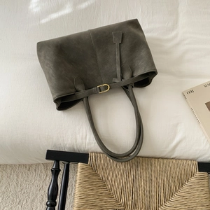 Deep grey green frosted suede tote bag with golden buckle on a vintage woven chair