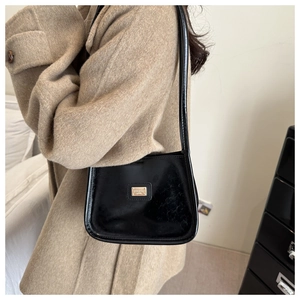 Détail d'un sac à bandoulière en cuir verni noir avec plaque logo métallique dorée