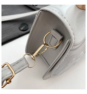 Detailed close-up of the golden metal hook and smooth gray leather of the crossbody bag