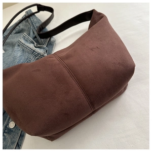 Detail of dark brown suede shoulder bag with dual stitching on a white fabric surface