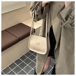 Detail of a beige leather shoulder bag with a gold metal plaque on a trench coat