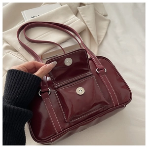 Detail of burgundy patent leather bag with white stitching and magnetic buckle closure