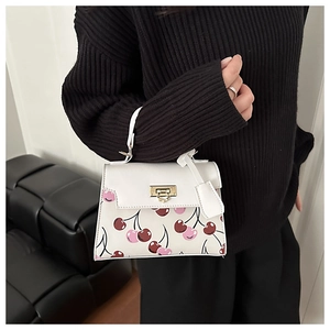 Détail d'un sac bandoulière blanc avec imprimé cerises et fermoir en métal doré