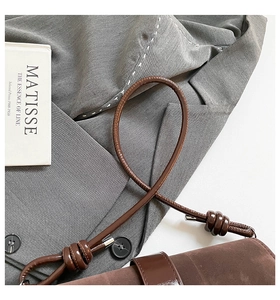 Close-up of brown suede shoulder bag featuring decorative knots and shiny patent leather trim