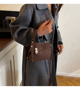 Brown leather crossbody bag with gold hardware shown on a coat for styling detail