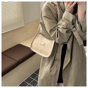 Sac à bandoulière en cuir beige avec détails dorés porté sur un trench-coat kaki classique