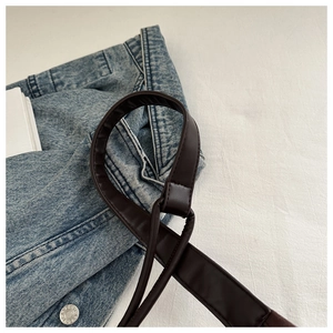 Detail of dark brown leather tote strap with fine stitching on denim jacket background