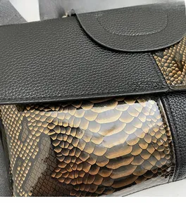Detailansicht von schwarzem Litschileder und goldener Schlangenhauttextur auf einer Tasche