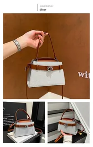 Detail of silver textured trapezoid bag with brown leather handles and metal buckle