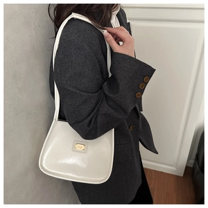 Détail d'un sac porté épaule blanc chic avec boucle dorée sur un blazer moderne