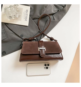 Detail of a vintage dark brown shoulder bag with silver buckle next to a smartphone