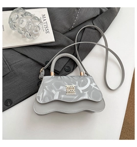 Detail of grey leather handbag with wavy base and gold logo on a textured background