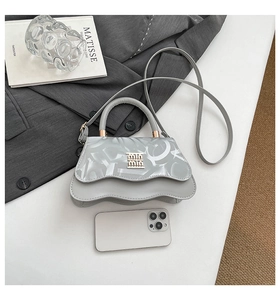 Detail of gray handbag with wavy edges, metallic brand buckle, and stylish shoulder strap