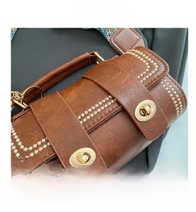 Detail of brown leather bag with wave stitching, gold oval twist lock, and printed strap