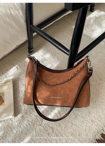 Détail d'un sac hobo en daim marron avec garniture en cuir et chaîne sur tapis