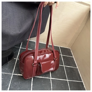 Detail of burgundy patent leather shoulder bag with white contrast stitching and front pocket