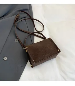 Detailed close-up of dark brown textured leather crossbody bag with gold rivet accents