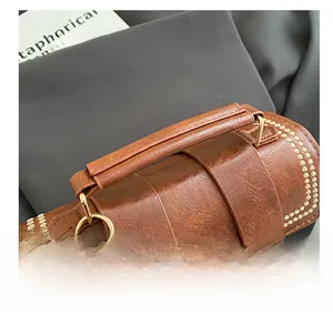 Close-up of vintage brown leather handbag handle with gold studs and textured finish