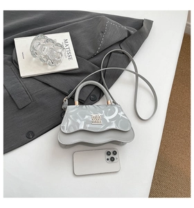 Detail view of light grey handbag with wavy flap and golden logo on a grey suit jacket