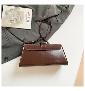Detail of dark brown leather baguette bag with suede stitching on grey blazer