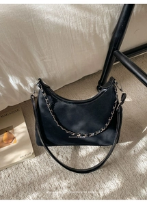 Détail du sac hobo croissant en daim noir avec chaîne argentée sur un tapis blanc