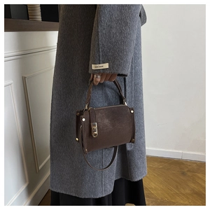 Detailed shot of brown pebbled leather texture and gold metal buckle on a shoulder bag