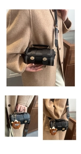 Detail of black cylinder bag with white studs, wide woven strap and plush charm pendant