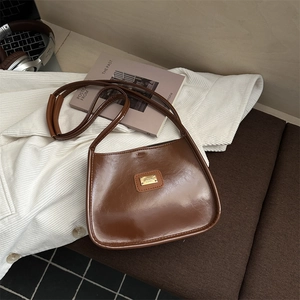 Sac à bandoulière en similicuir marron avec logo doré sur fond de chemise blanche