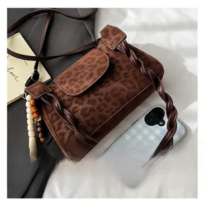 Detail of leopard print shoulder bag featuring a woven strap and tassel charm decoration
