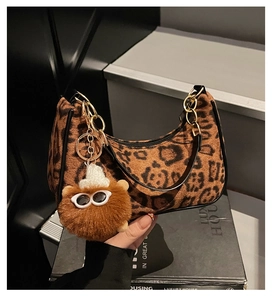 Close-up of leopard print crescent bag with gold chain and plush monster charm detail