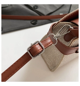 Close-up of the silver hardware and brown leather strap on a textured woven handbag