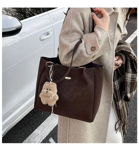 Close-up of a dark brown leather tote bag featuring a cute plush dog pendant charm