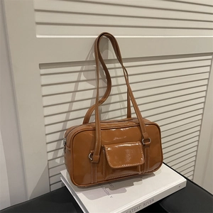 Brown patent leather shoulder bag with white stitching on a minimalist book stand