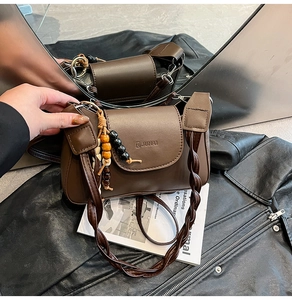 Close-up of brown leather bag with braided strap and ethnic beaded charm decoration