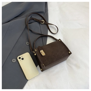 Detail of dark brown suede shoulder bag with golden twist lock and textured finish