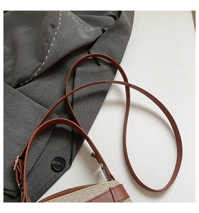 Detail of beige textured fabric and brown leather strap with silver buckle on crossbody bag