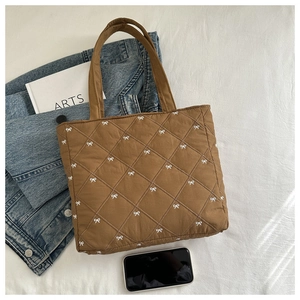 Vista piana della borsa tote marrone trapuntata con ricami a fiocco bianco e accessori