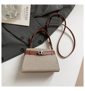 Detail of woven beige handbag with brown leather strap and silver buckle on white surface