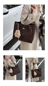 Detail of dark brown suede tote bag with plush bear charm in an outdoor street setting