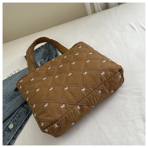 Dettaglio borsa shopper marrone trapuntata con fiocchi bianchi e ricamo a rombi