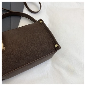 Detail of dark brown textured leather shoulder bag with golden rivets and metal lock