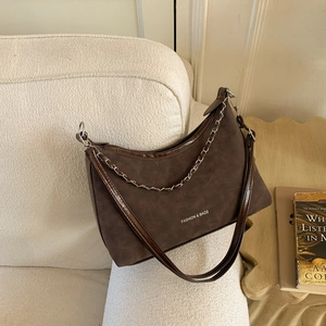 Sac demi-lune en daim marron foncé avec chaîne argentée sur canapé en polaire