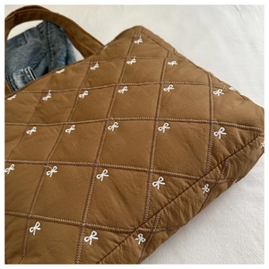Dettaglio della borsa tote marrone trapuntata con ricami di fiocchi bianchi e texture