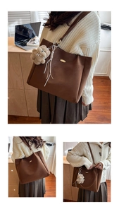 Detail of brown tote bag with metal logo, plush bear charm and woven tassel accent